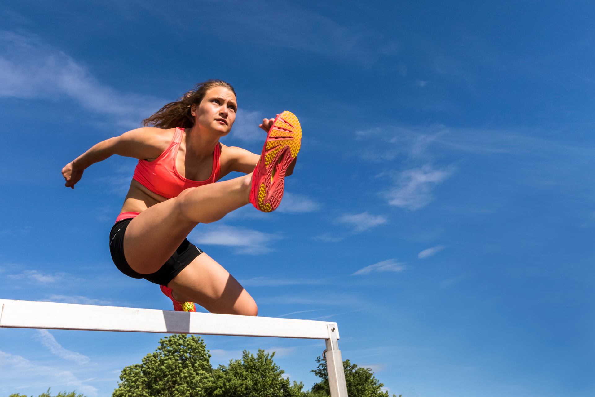 Athlete clearing a hurdle in mid-air against a blue sky